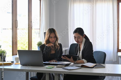 Two attractive businesswomen discussing project strategy together at modern office.