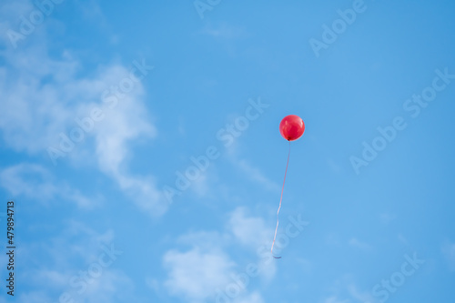 A red balloon flying under the blue sky and white clouds