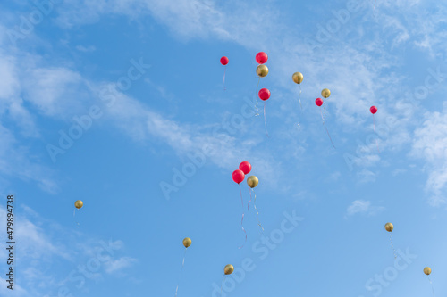 Many red and gold balloons fly under the blue sky and white clouds