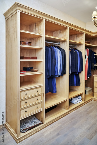 Stylish walk in closet with furniture of maple solid and veneer wood for clothes storage with crown molding in apartment