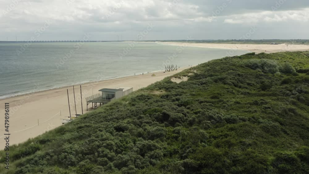 Aerial shot flying over green dunes and past a beach pavilion, towards the sea on an overcast day Aerial shot flying over green dunes and past a beach pavilion, towards the sea on an overcast day