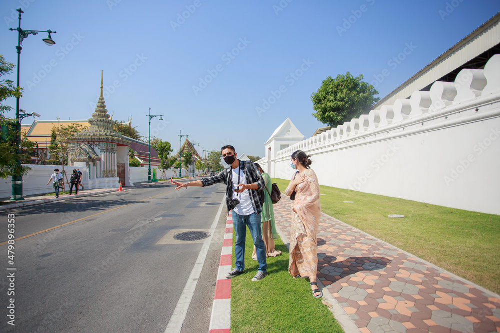 Obraz premium Three South Asian tourists with cameras happily hitchhiking the road behind Wat Pho during their long weekend happily. in Bangkok, Thailand
