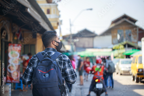 A South Asian tourist wearing a camera-printed shirt and backpack walks happily on a long weekend. in Bangkok, Thailand