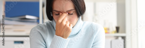 Painful depressed woman sits with eyes closed at workplace photo