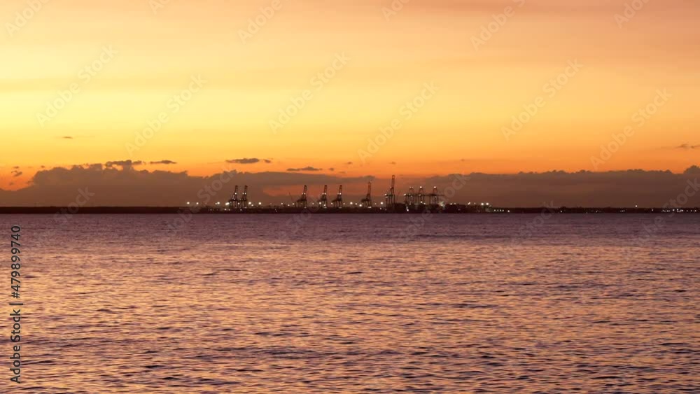 Cargo port at sunset. Cranes unload containers, view from the sea Cargo port at sunset. Cranes unload containers, view from the sea