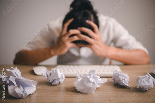 Businessman sitting with head in hands at desk covered crumpled papers. Office worker tired of too much difficult unproductive work. Stressed male entrepreneur has no idea what to do with problem