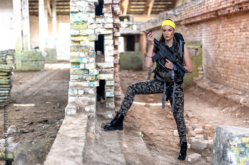 Woman in paintball club with gun on her hands and backpack play photo