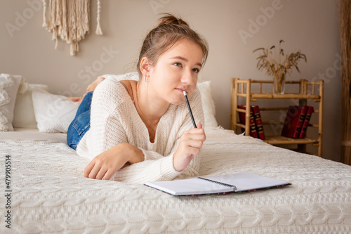Closeup portrait of a relaxed young girl writing book while lying on the bed