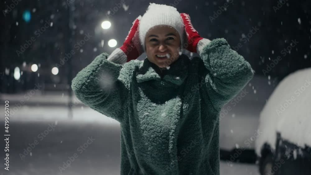 Cinematic shot of carefree happy smiling young woman wearing warm hat is excited and amazed with snowfall in a festive winter evening.Concept of winter holidays, freedom, happiness Cinematic shot of carefree happy smiling young woman wearing warm hat is excited and amazed with snowfall in a festive winter evening.Concept of winter holidays, freedom, happiness