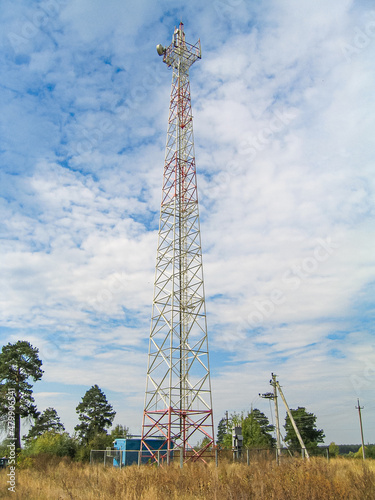 High lattice cell tower with antennas on top, in an open field against a sky with clouds