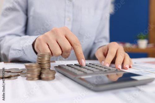 Female count on silver calculator, cash coins on office desk