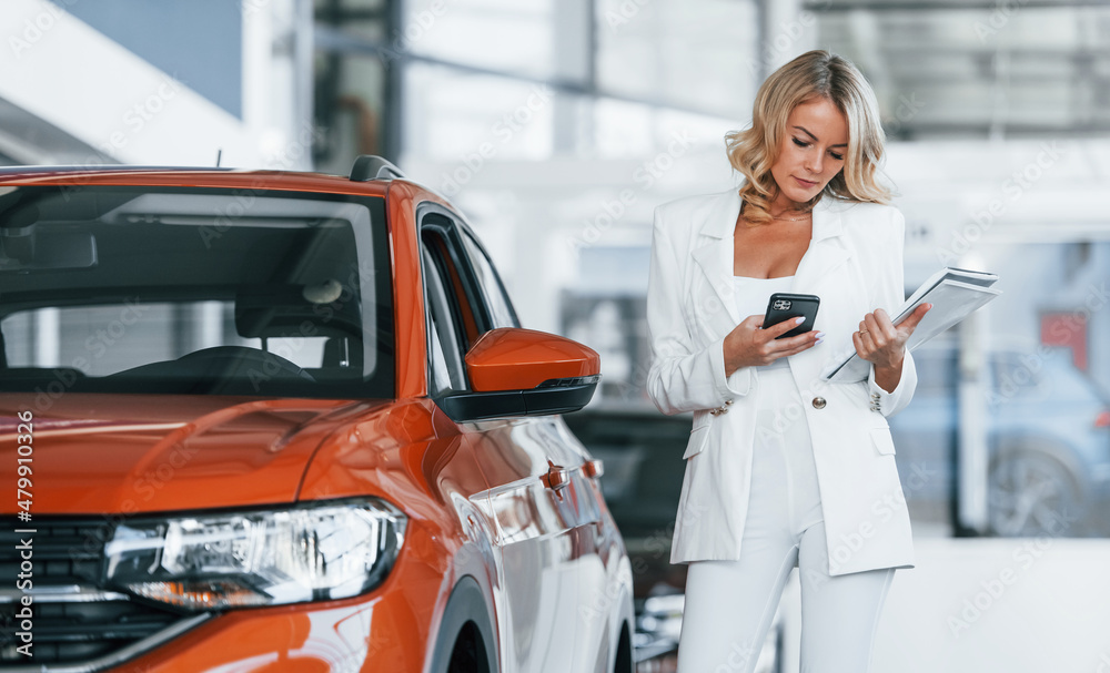 Fototapeta premium Holding phone. Woman in formal clothes is indoors in the autosalon