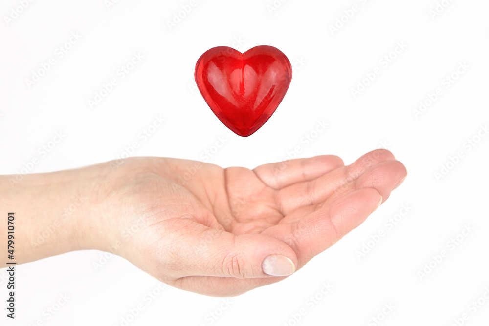 Glass heart over a woman's hand on a light background.
