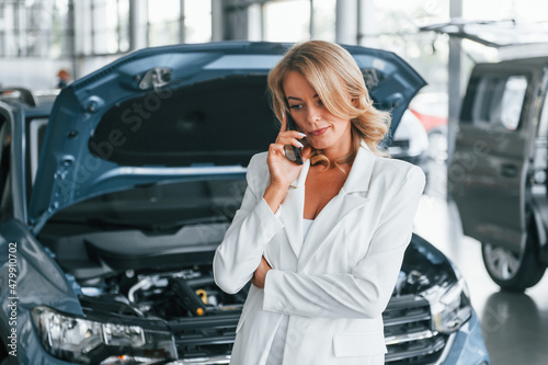 Talking by phone. Woman in formal clothes is indoors in the autosalon © standret