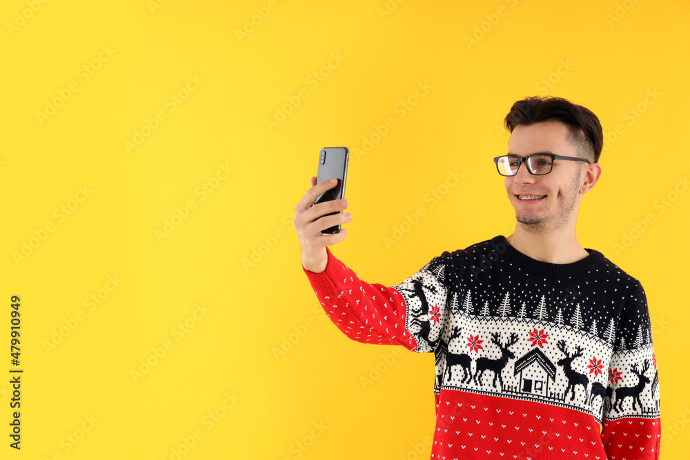 Guy in Christmas sweater with phone on yellow background Guy in Christmas sweater with phone on yellow background