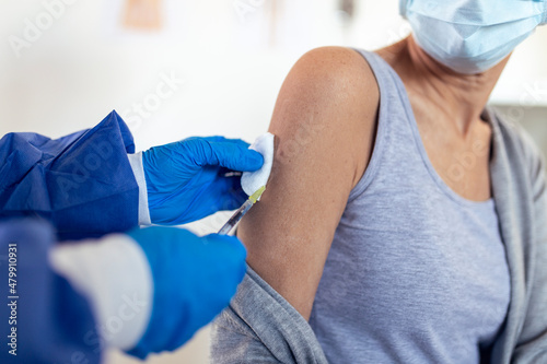 Senior woman patient sitting in a medical clinic and is being given the Covid 19 vaccine in his shoulder by a female doctor  both wearing protective face masks