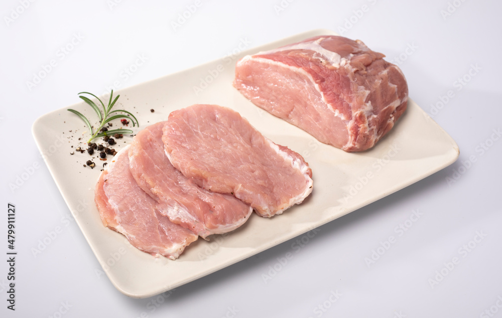 Fresh raw meat, pork loin in cross-section and sliced in chops on a white plate, isolated on white. A packshot photo.