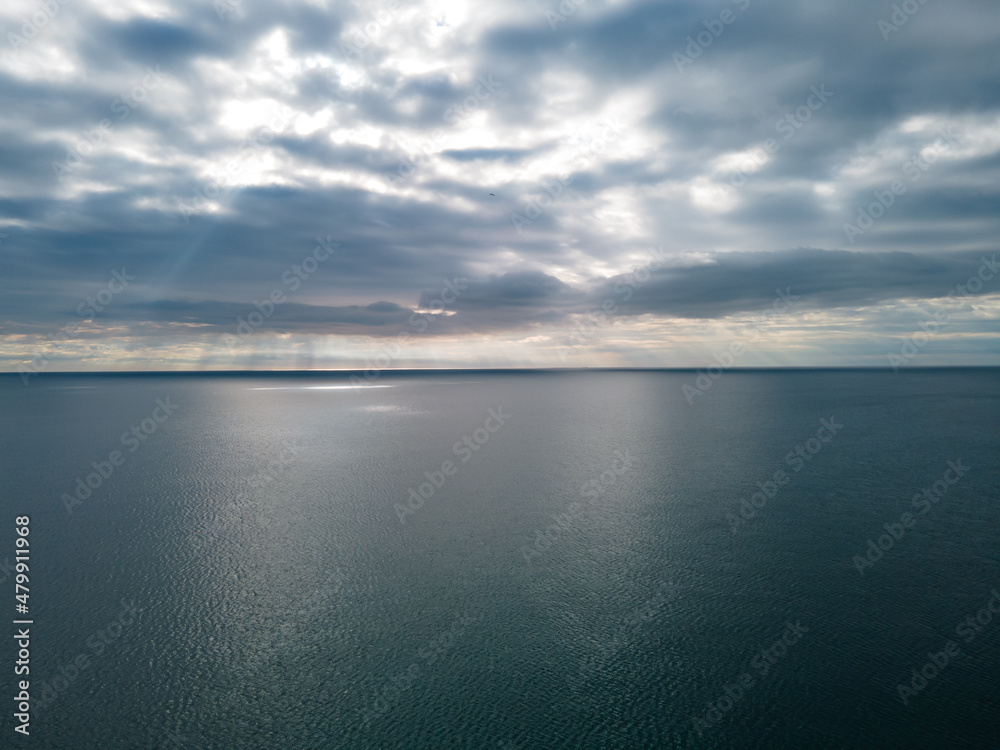 Aerial view over the sea with beautiful gray clouds illuminated by the sun