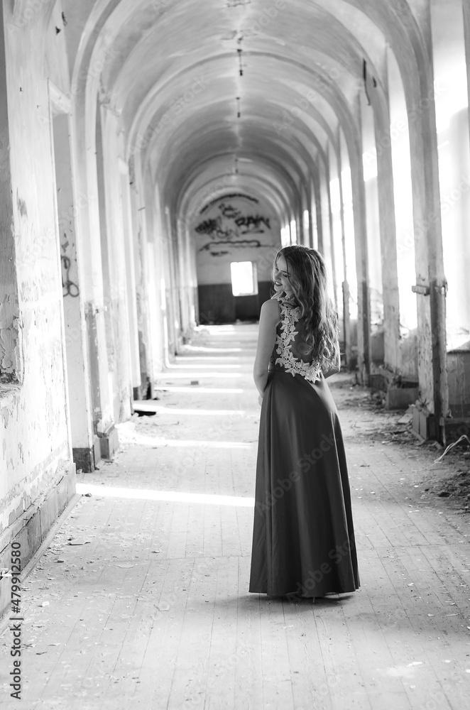 Young beautiful short hair blonde woman in black climbing the stairs, black and white photo. Side view of elegant romantic mysterious lady with movie star look in interior with bricks walls