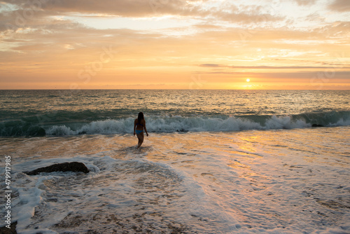 a girl with long hair stands in the waves of the sea against a beautiful sunset