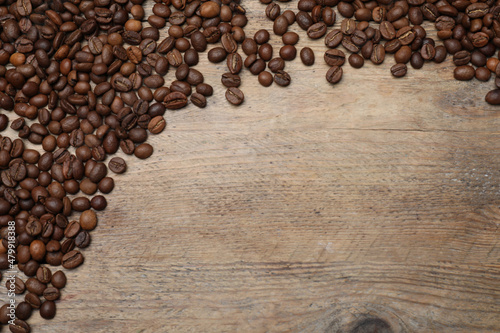 Many roasted coffee beans on wooden table, flat lay. Space for text