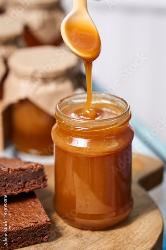 homemade caramel in a jar. caramel deliciously drips down a spoon into a jar