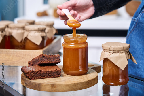 a woman s hand holds a spoon on which homemade caramel flows into a jar