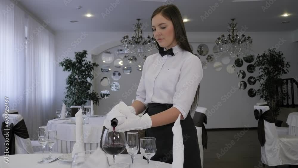 Close-up of a professional waiter in white gloves pouring red wine into a glass in a restaurant.