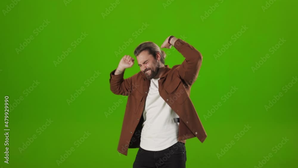 Positive young man with stylish beard and haircut dancing happily over green studio background. Caucasian male hipster in casual outfit taking fun during free time. Positive young man with stylish beard and haircut dancing happily over green studio background. Caucasian male hipster in casual outfit taking fun during free time.