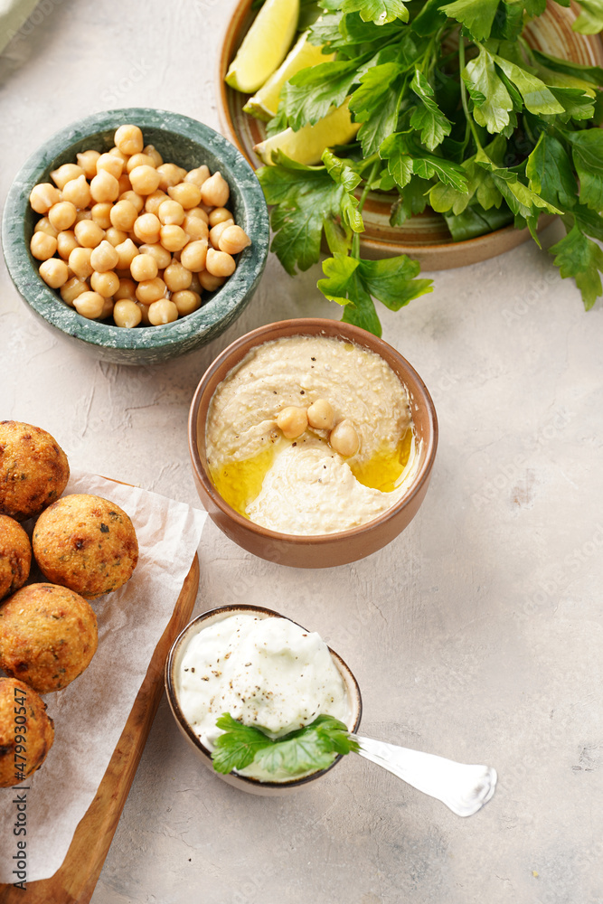Traditional oriental chickpea deep fried falafel on a wooden board, tzatziki yoghurt sauce, hummus, fresh lime and green cilantro on light surface