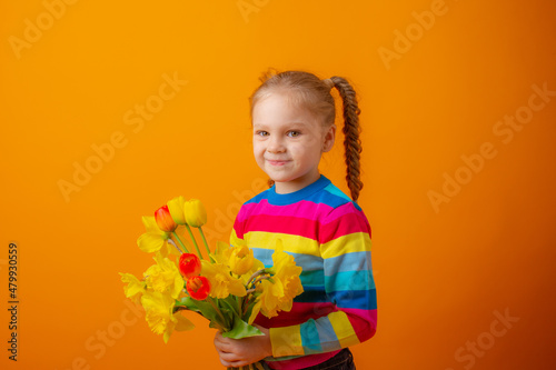 a cute little girl in a multicolored sweater holds a bouquet of spring flowers on a yellow background
