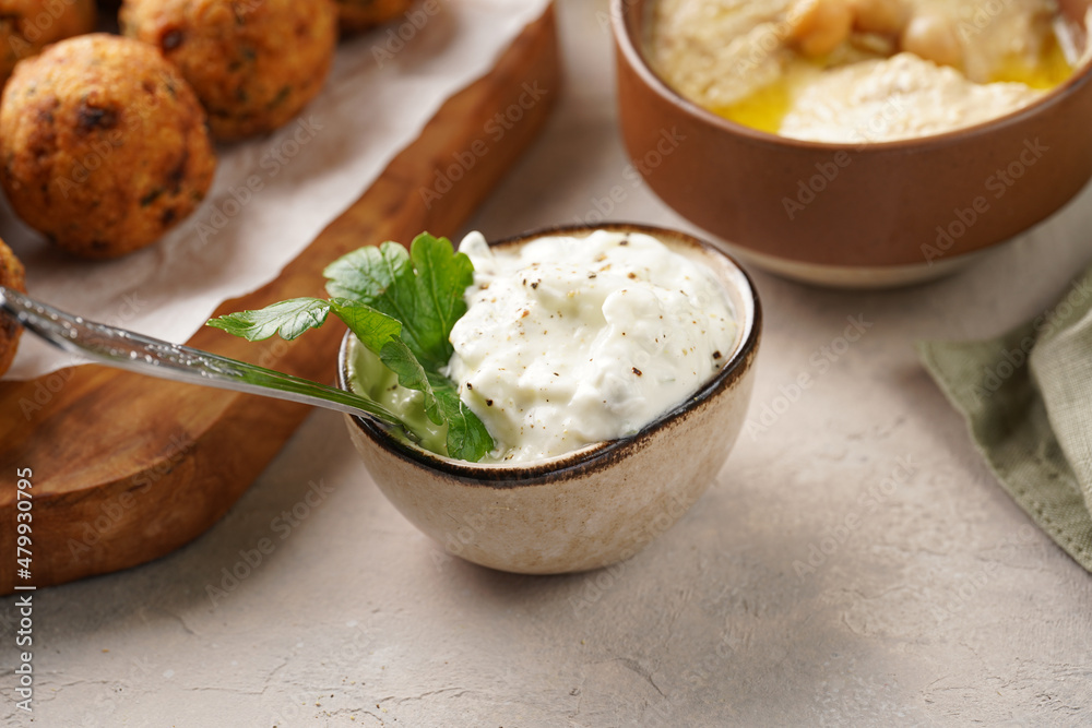 Traditional oriental chickpea deep fried falafel on a wooden board, tzatziki yoghurt sauce, hummus, fresh lime and green cilantro on light surface Traditional oriental chickpea deep fried falafel on a wooden board, tzatziki yoghurt sauce, hummus, fresh lime and green cilantro on light surface