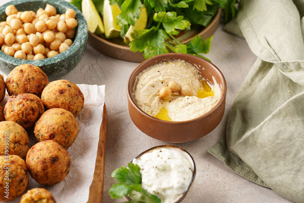 Traditional oriental chickpea deep fried falafel on a wooden board, tzatziki yoghurt sauce, hummus, fresh lime and green cilantro on light surface