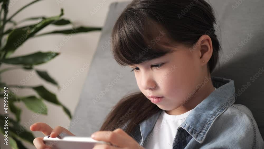 Cute little kid girl holding smart phone enjoying using mobile apps, playing games at home. Small child learning in cellphone, watching video. Mobile technology concept. Cute little kid girl holding smart phone enjoying using mobile apps, playing games at home. Small child learning in cellphone, watching video. Mobile technology concept.