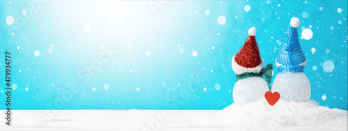 Winter snow snowman background panoramic banner panorama holiday greeting card - Little cute Snowman and red heart from the back sits on snow in snowy landscape with snowflakes blue sky and sunshine © Corri Seizinger