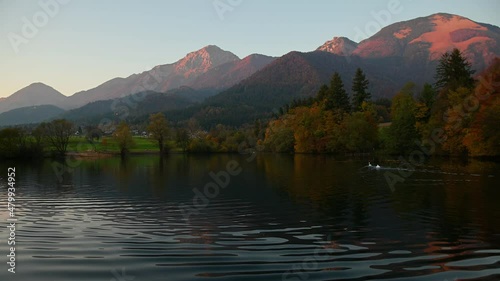 Beautiful small pond under the mountains. Pristine lake in Preddvor, Slovenia. Alps in the background. Colorful autumn season. Reflection of the Alps in calm water. Static shot, real time photo