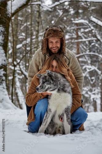 Young couple smiling and having fun in winter park with their husky dog