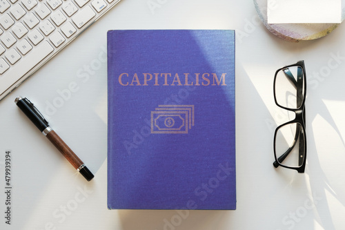 Book on capitalism illustration. Office desk table lit by evening sun. Top view, flat lay. photo