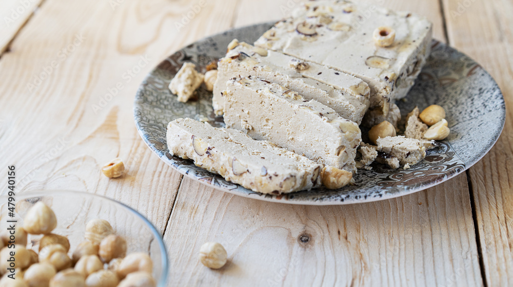 Fototapeta premium Halwa with hazelnuts on grey plate and wooden background 
