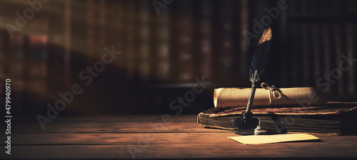 old quill pen with inkwell and papers on wooden desk against vintage bookcase. retro style. banner copy space photo