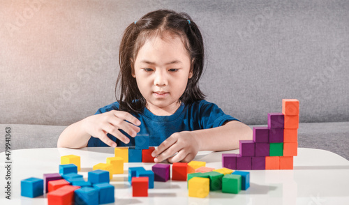 Asian girl plays with small wooden colorful toy blocks at home or kindergarten. A Girl enjoys playing with construction blocks for toddler kids. Education Development Construction creative toys Idea
