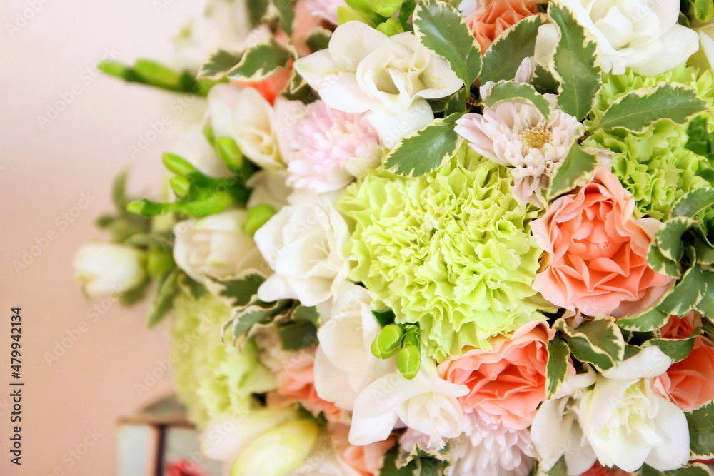 Round bouquet with white freesia flower, green dianthus, peach roses, light chrysanthemum and fresh greens. Bridal bouquet and wood on pink background. Front view, closeup Round bouquet with white freesia flower, green dianthus, peach roses, light chrysanthemum and fresh greens. Bridal bouquet and wood on pink background. Front view, closeup