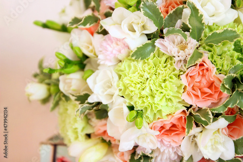 Round bouquet with white freesia flower, green dianthus, peach roses, light chrysanthemum and fresh greens. Bridal bouquet and wood on pink background. Front view, closeup