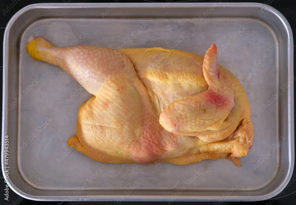 Halved uncooked chicken laid in a roasting tin rady for the oven - obrazy, fototapety, plakaty 