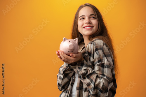 Teen girl with piggy bank on yellow background.