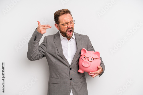 middle age man looking unhappy and stressed, suicide gesture making gun sign. businessman and a pigy bank concept photo