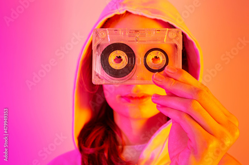 Teenager girl holding old cassette tape - pink and orange background, pop art style © pinkyone