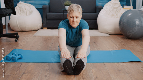 Senior woman stretching in aerobics position on yoga mat. Aged person doing physical exercise and training for wellness and healthcare. Pensioner doing gymnastics workout at home. photo