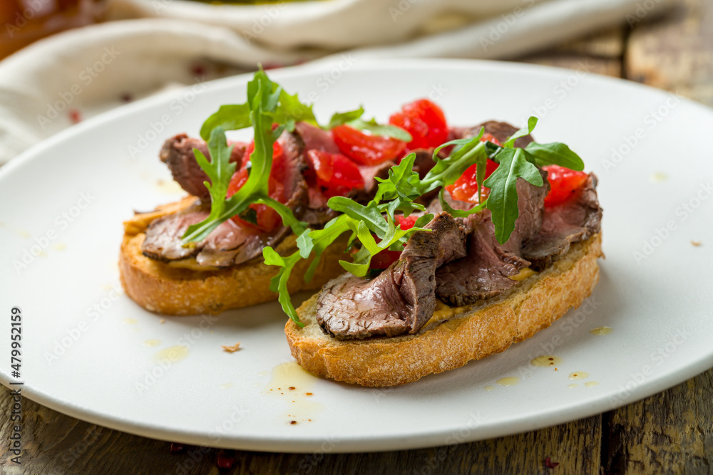 Bruschetta with roast beef, tomatoes and aragula on white plate Bruschetta with roast beef, tomatoes and aragula on white plate