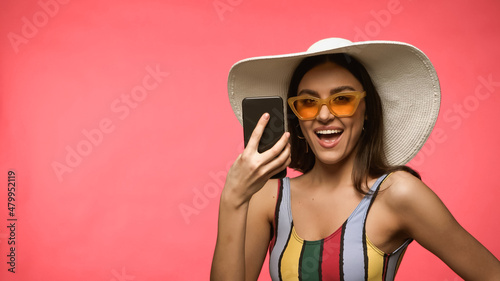 Excited woman in swimsuit holding cellphone isolated on pink.